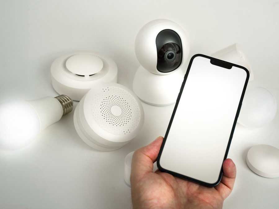 Mão segurando um celular ao lado de equipamentos de casa inteligente